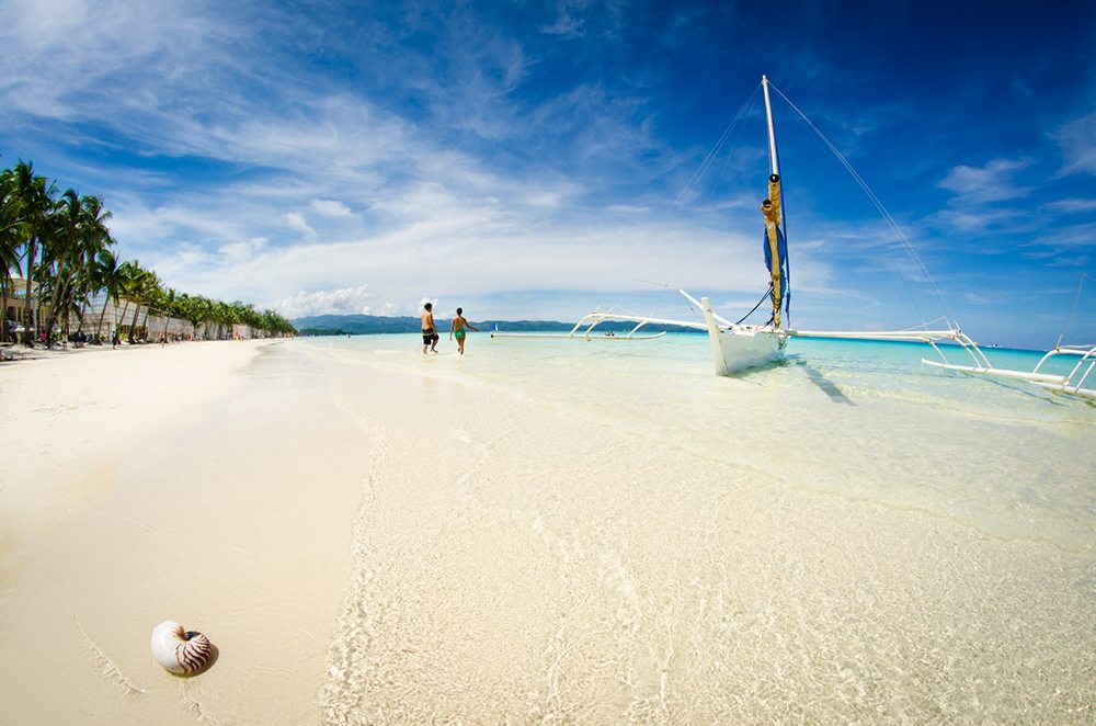 Dva lidé na pláži na ostrově Boracay vedle tradiční loďky.