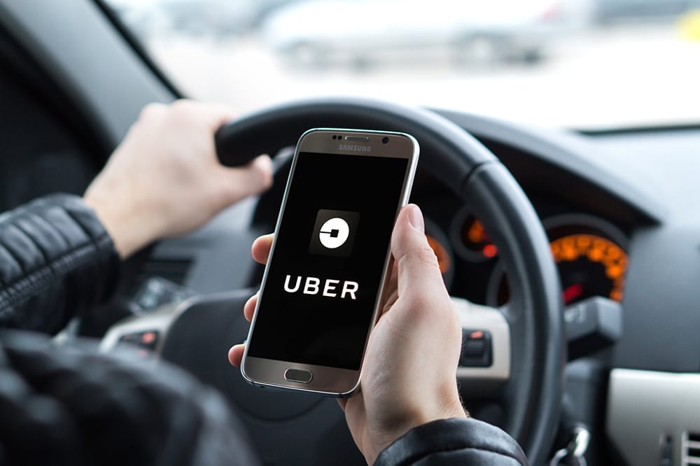 Muž za volantem držící mobilní telefon v ruce, s aplikací UBER.